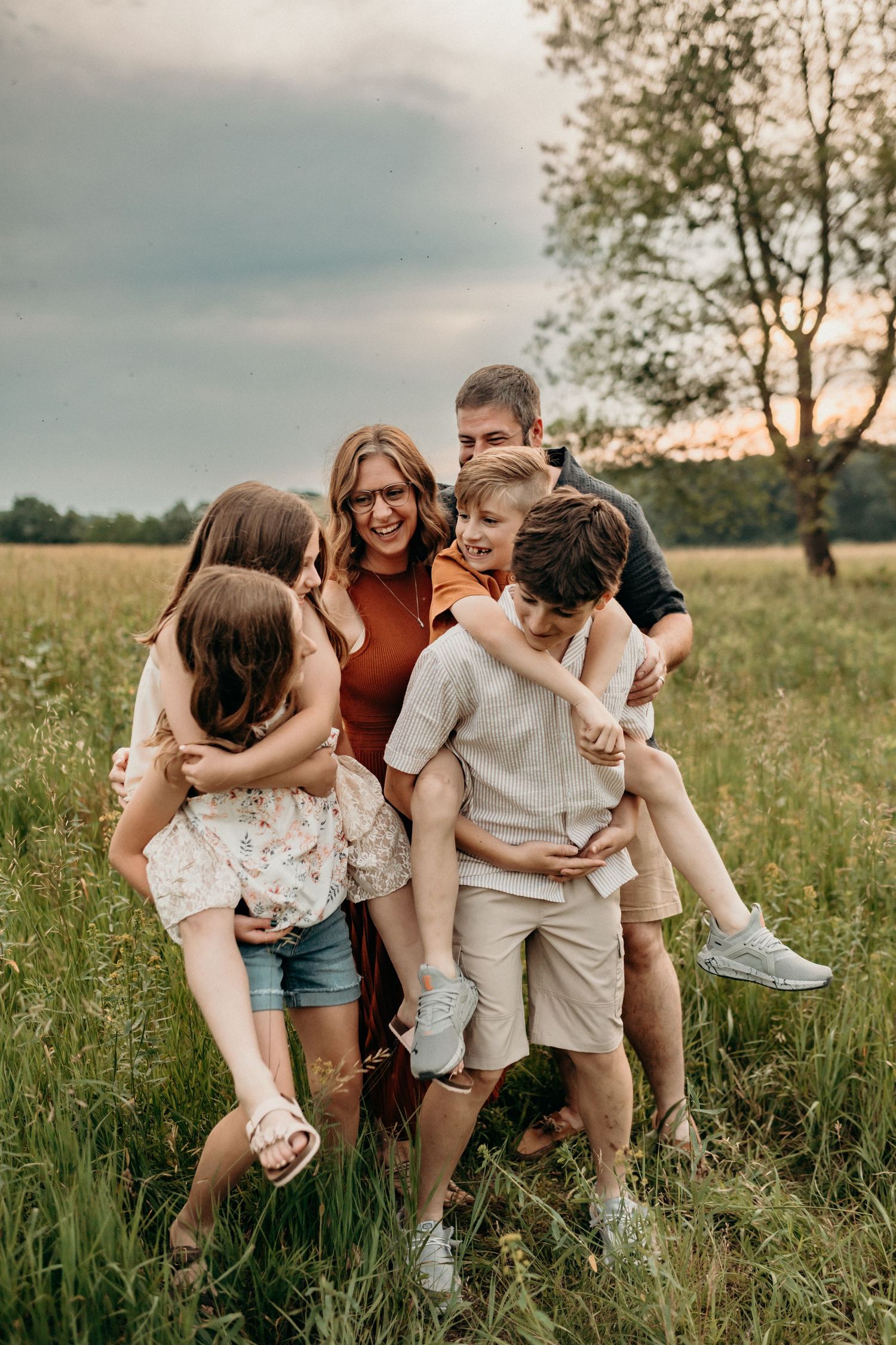 A group of loved ones share a joyful candid moment together in a golden sunlit meadow during sunset.