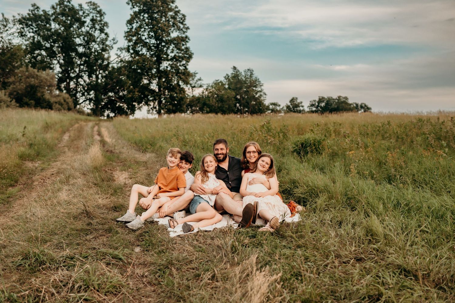 People enjoying a sunny afternoon lounging together on a grassy hillside path surrounded by trees.
