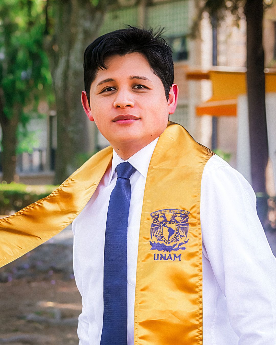 A student wearing a blue tie and yellow UNAM vest stands outdoors on a college campus.