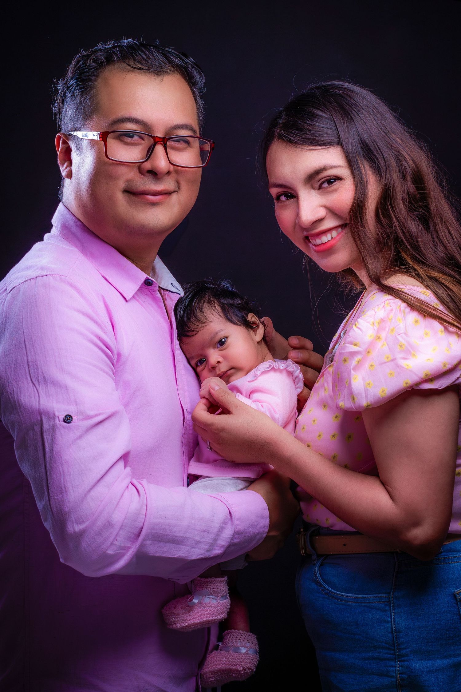 Family portrait with pink lighting and dark background.