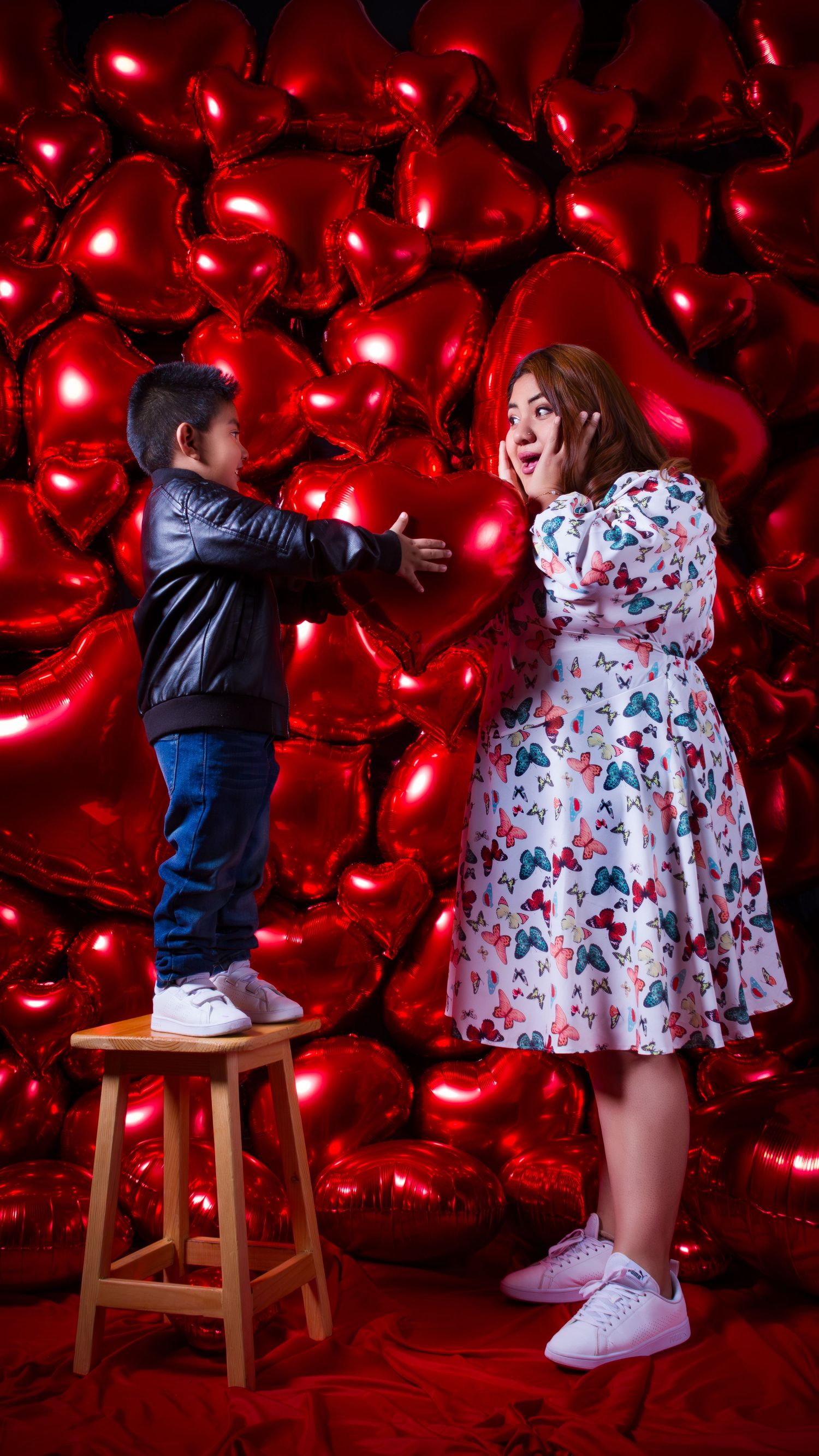 Romantic portrait against red heart balloons backdrop with floral dress and casual attire.