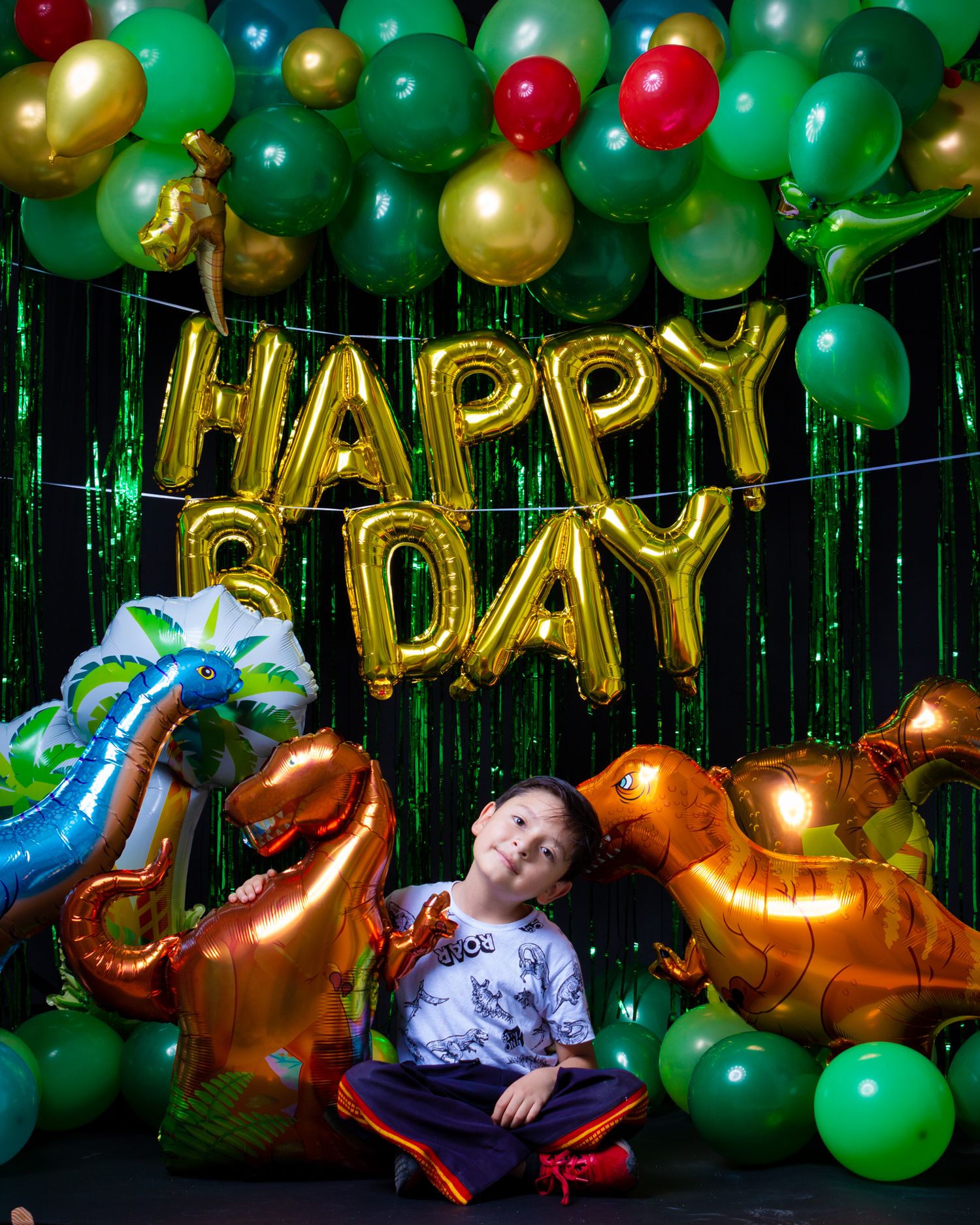 Child reclines among colorful balloons under gold Happy Bday sign.