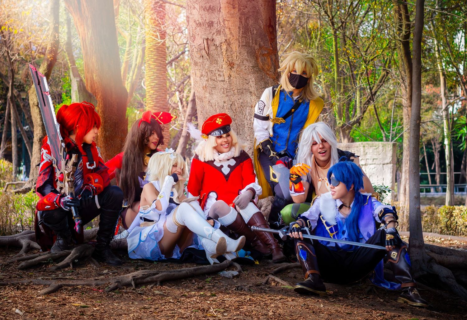 Fantasy cosplay group gathered under trees with sunlight streaming through branches.