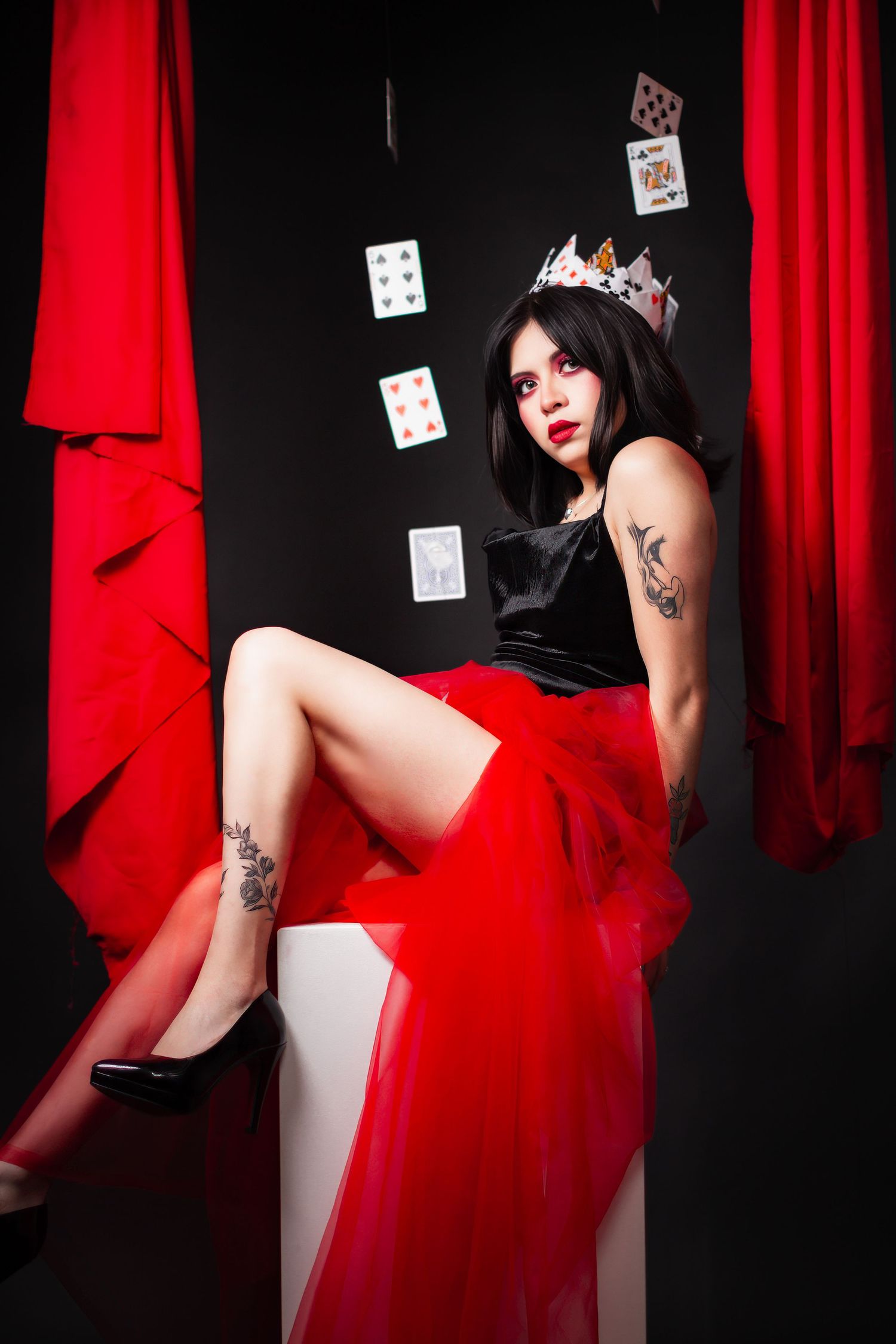 Artistic portrait with playing cards and red curtains in dramatic lighting.