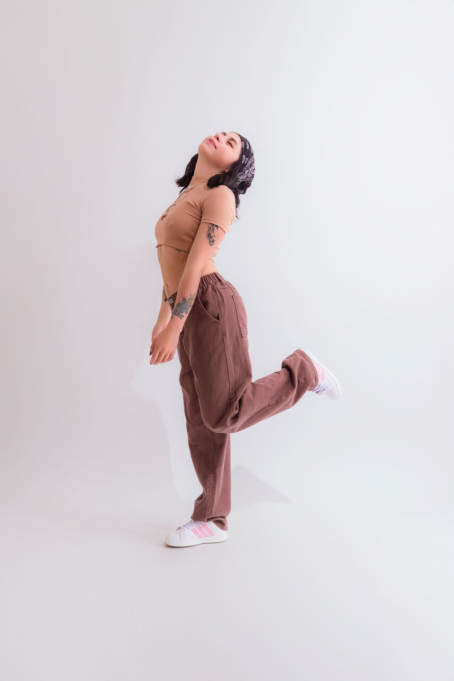 Dynamic pose of a dancer in brown pants and tan top against white background.
