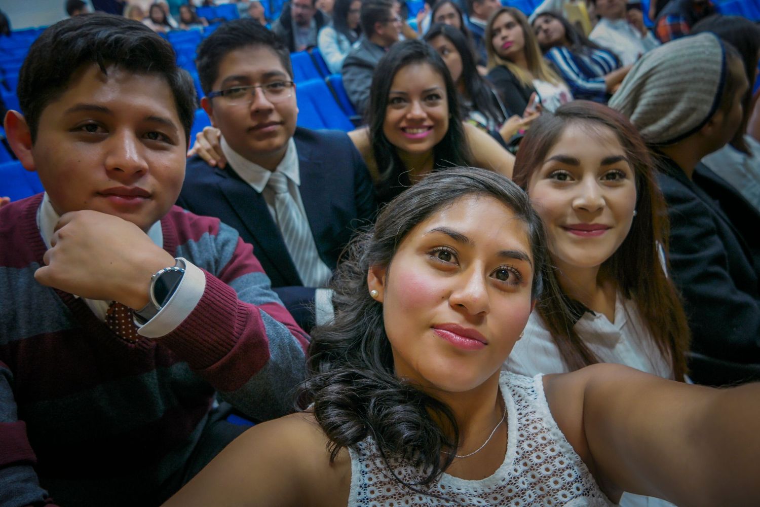 Group of friends taking a selfie together in crowded auditorium with blue seats.