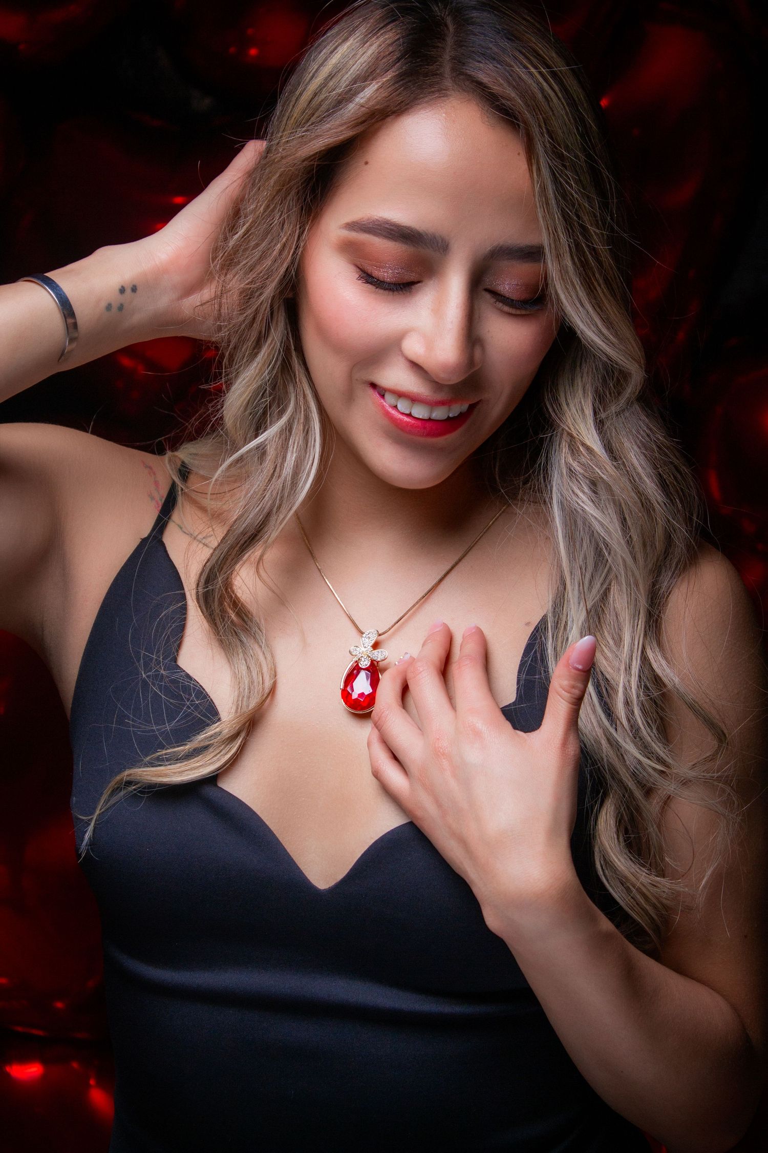 Glamour portrait of person in black dress holding red pendant necklace.