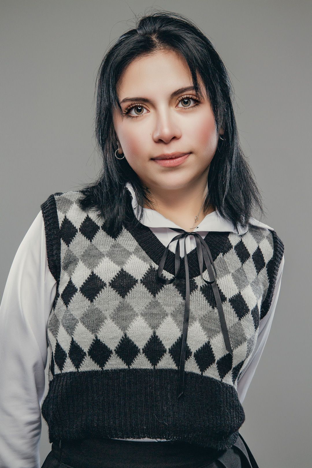 Studio portrait in classic argyle vest and white shirt against gray background.