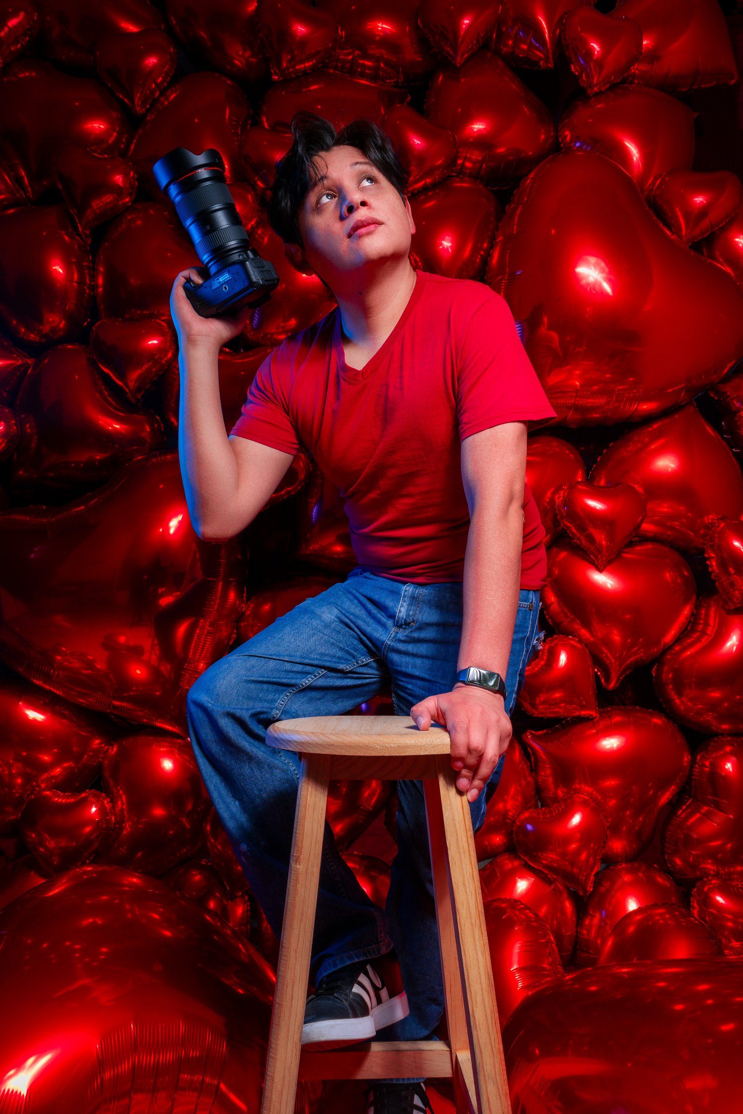 Creative portrait of photographer holding camera against glowing red heart background.