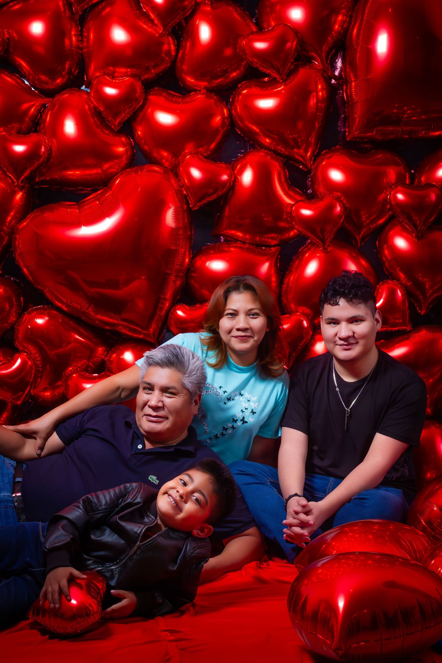 Family group lounging among large red heart-shaped balloons in festive photoshoot.