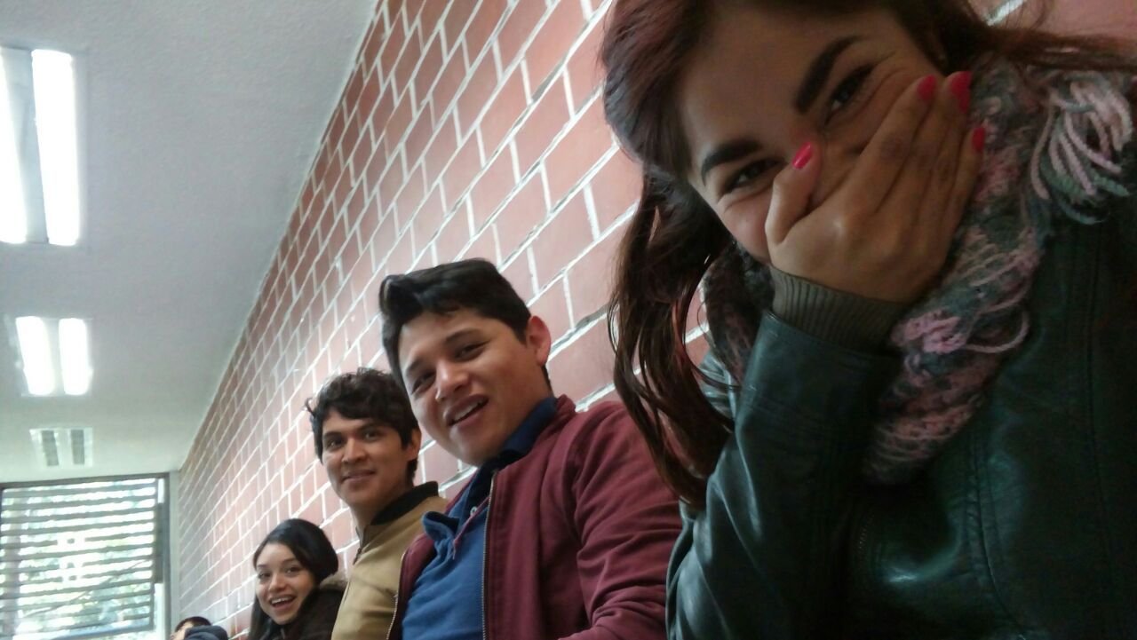 Students sitting together against brick wall in a hallway.
