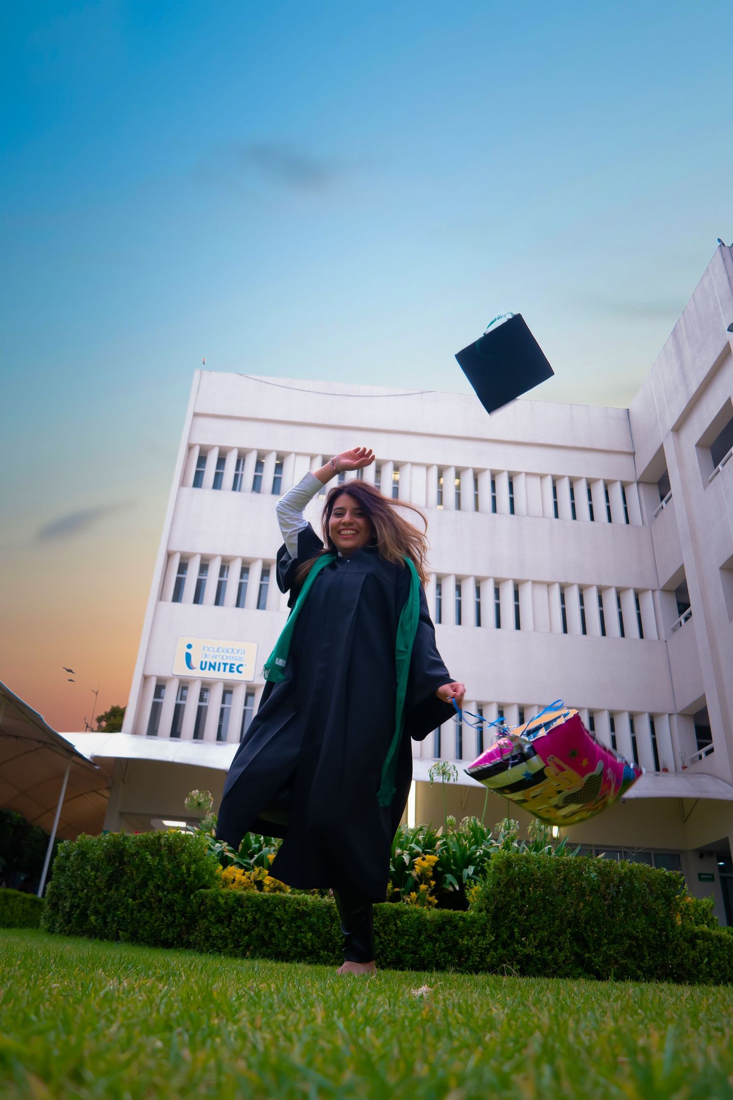 Graduation celebration photo with cap toss against white building and blue sky.