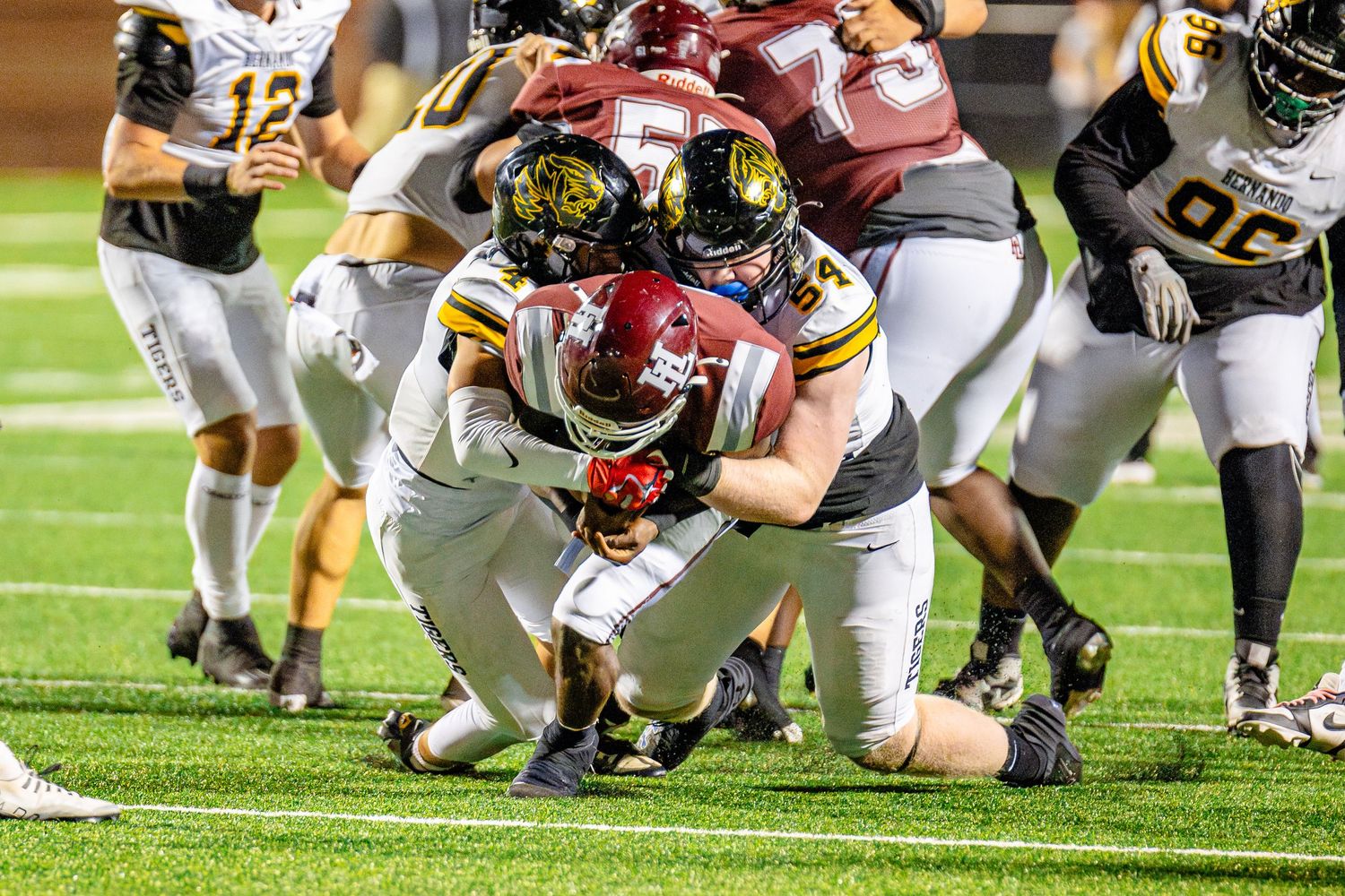 Football players pile up during a tackle at a nighttime game on the field.