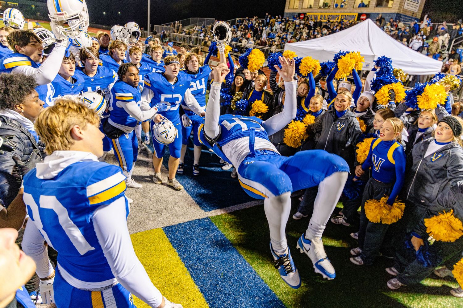 Cheerleaders in blue and white uniforms perform at a school sporting event alongside large crowd of supporters.