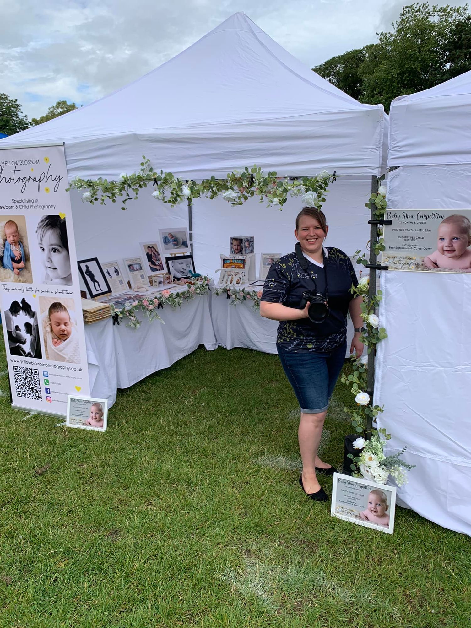 Photography booth display with white tent, floral decorations and sample photos at outdoor event.