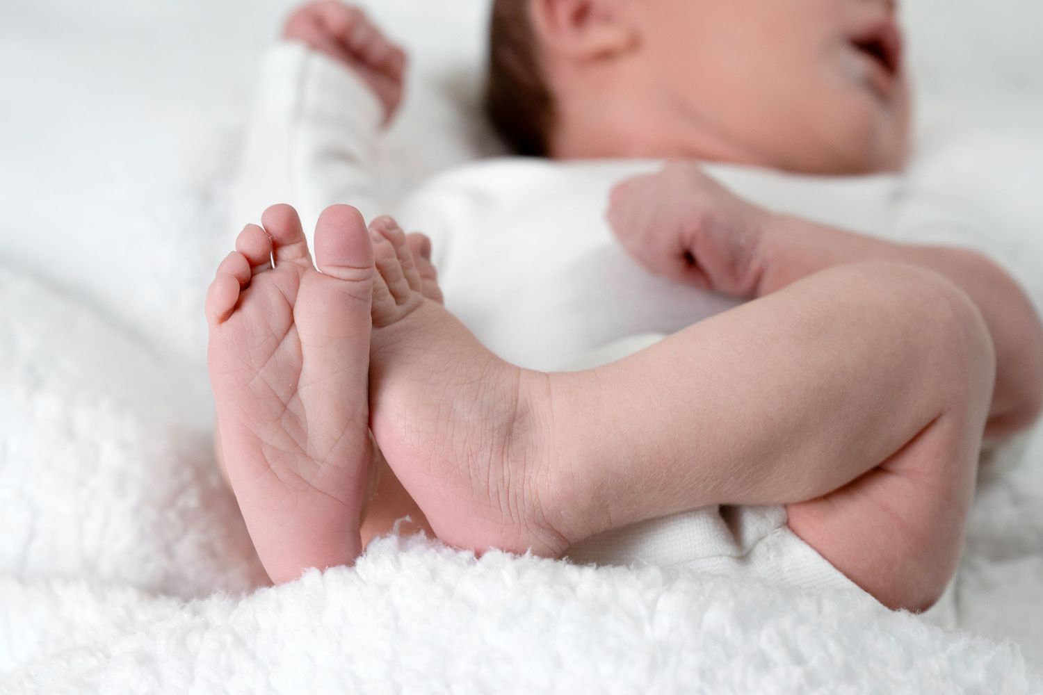 Close-up of tiny newborn feet resting on soft white textured blanket.