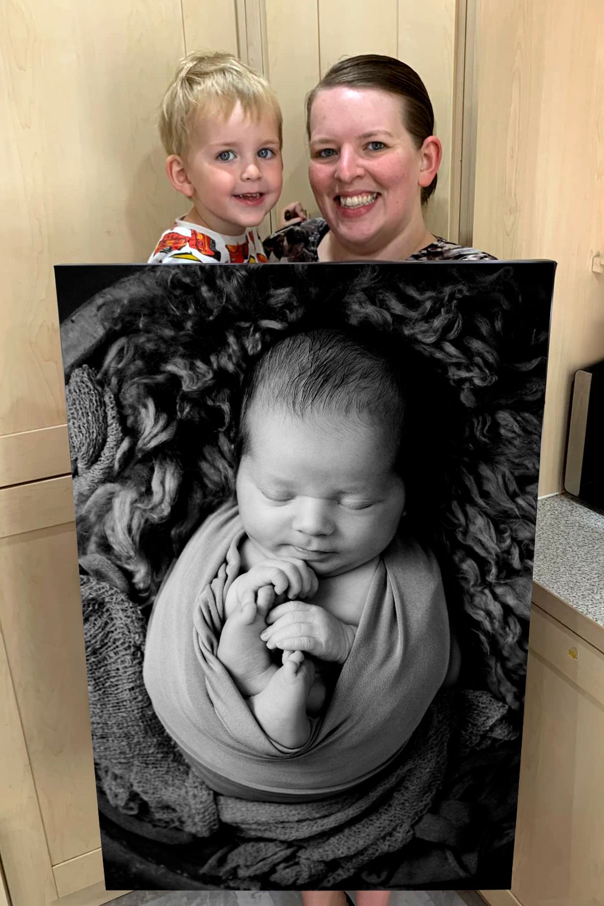 Portrait showing a framed black and white newborn photo being held up.