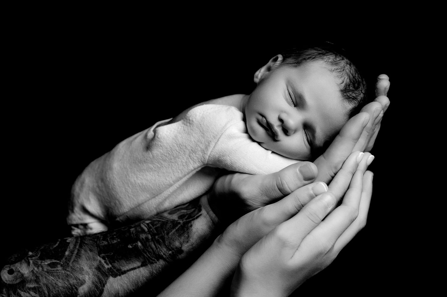 Peaceful newborn baby sleeping on supportive hands in black and white.
