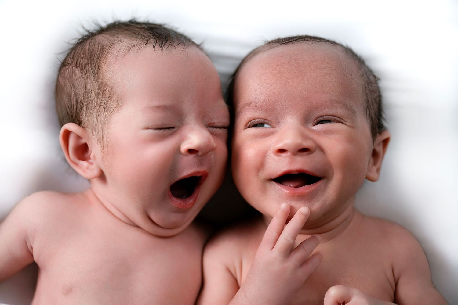 Two laughing babies laying side by side on white background.