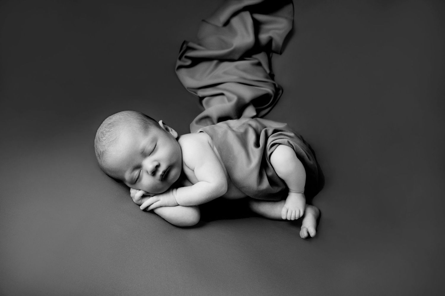 Black and white studio portrait of newborn baby with flowing fabric backdrop.