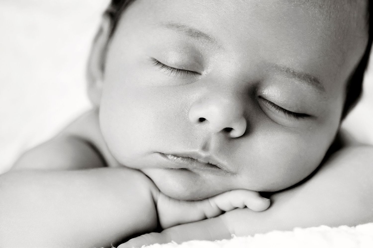 Serene black and white portrait of sleeping infant resting on folded arms.