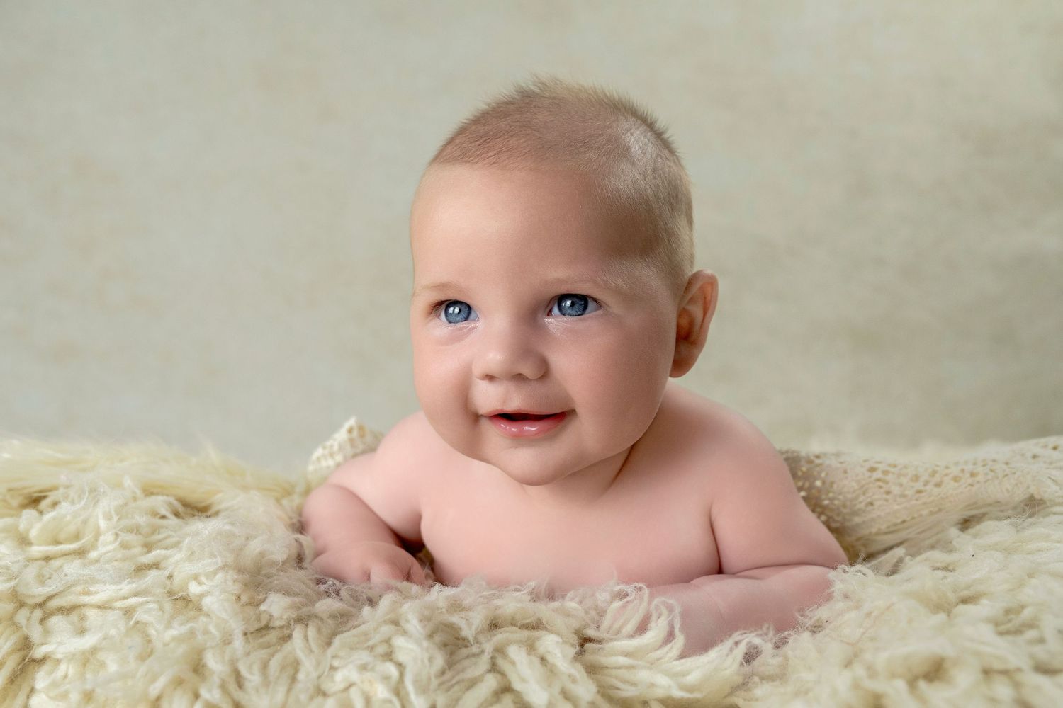 Baby laying on cream colored furry blanket smiling at camera.