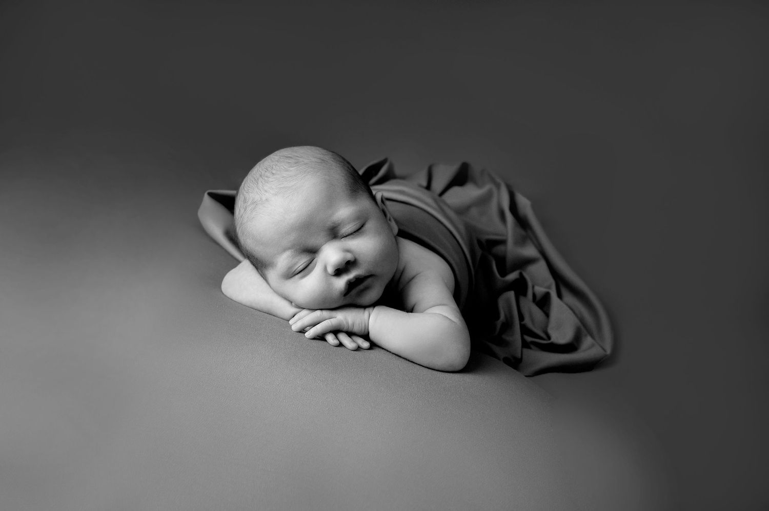 Black and white portrait of sleeping newborn in soft fabric with gentle lighting.