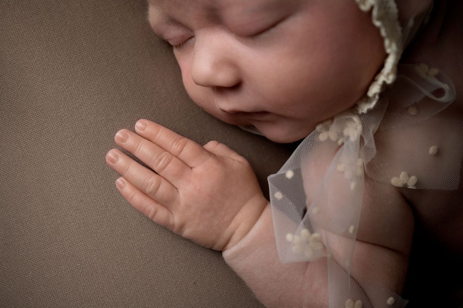 Close-up of sleeping newborn's hands with delicate lace details.