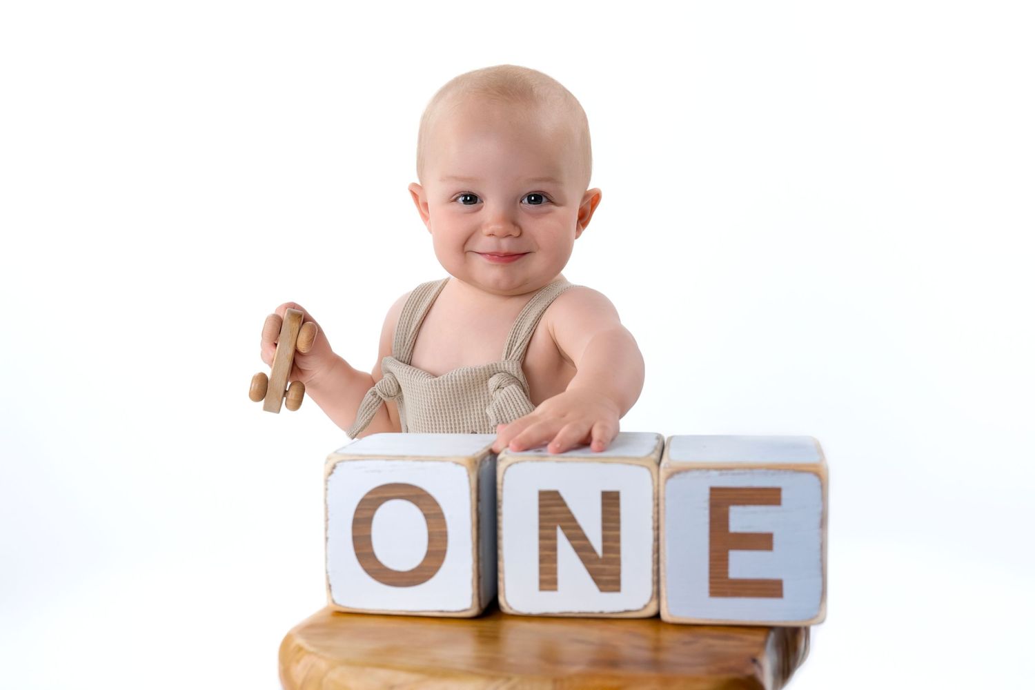 Baby in tan outfit poses with wooden blocks spelling ONE during milestone photo session.