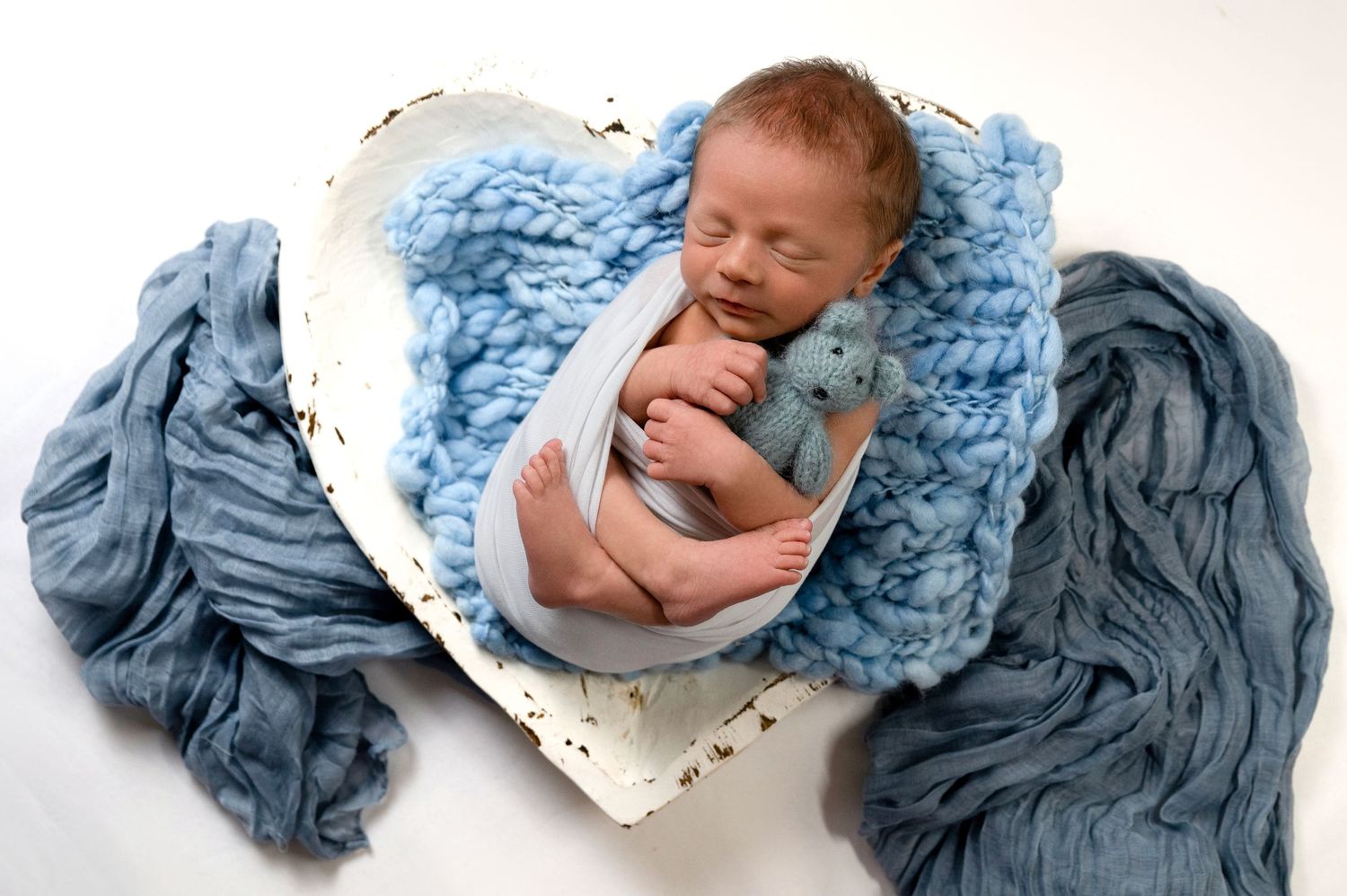 Sleeping newborn wrapped in soft blue knitted blanket during professional photo session.