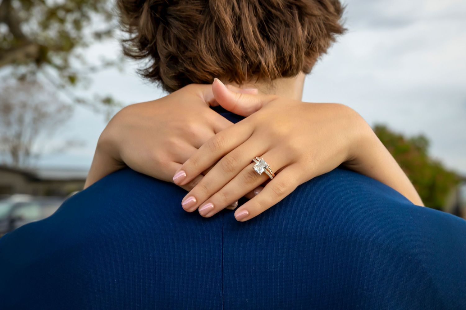 emerald cut diamond ring on bride's hand around groom's neck