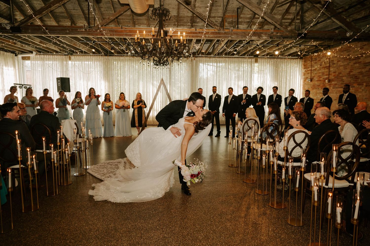 A dramatic wedding ceremony moment captured in a rustic industrial venue with exposed beams and romantic lighting.