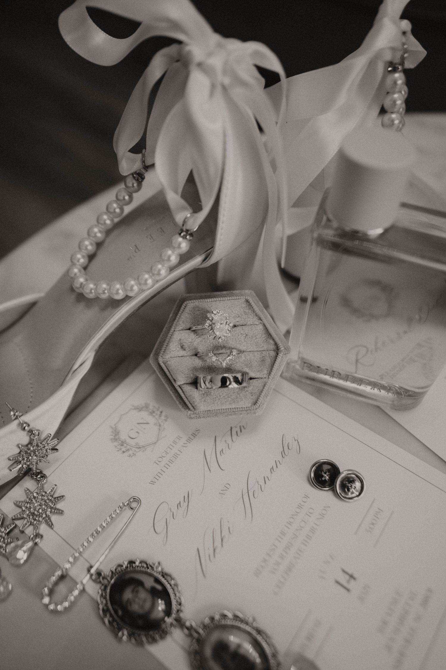 Black and white details of wedding accessories including invitations, pearls, and vintage jewelry laid out on a white surface.