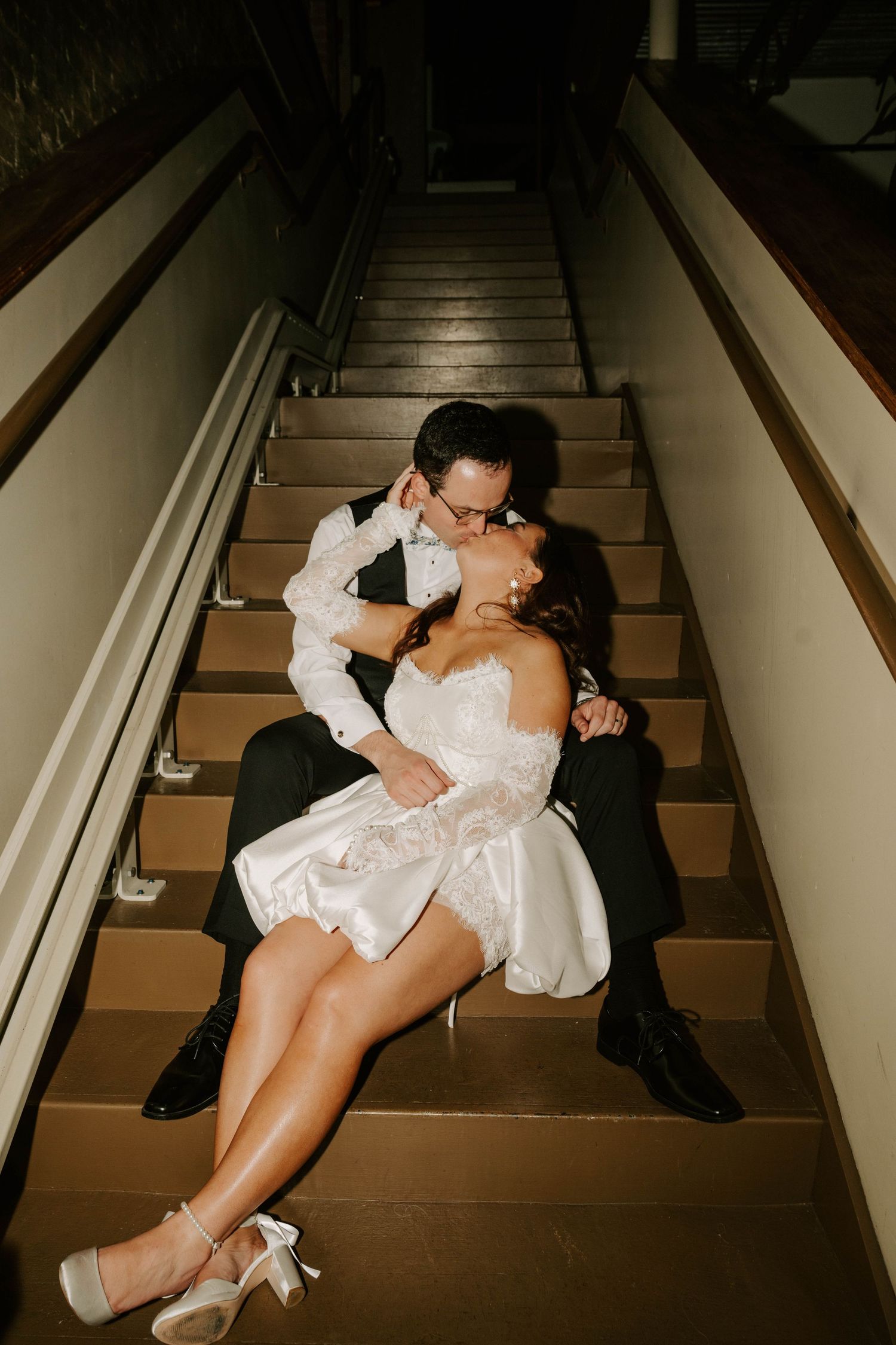 A couple shares intimate moments on dimly lit stairs in a romantic sequence of bridal photos.