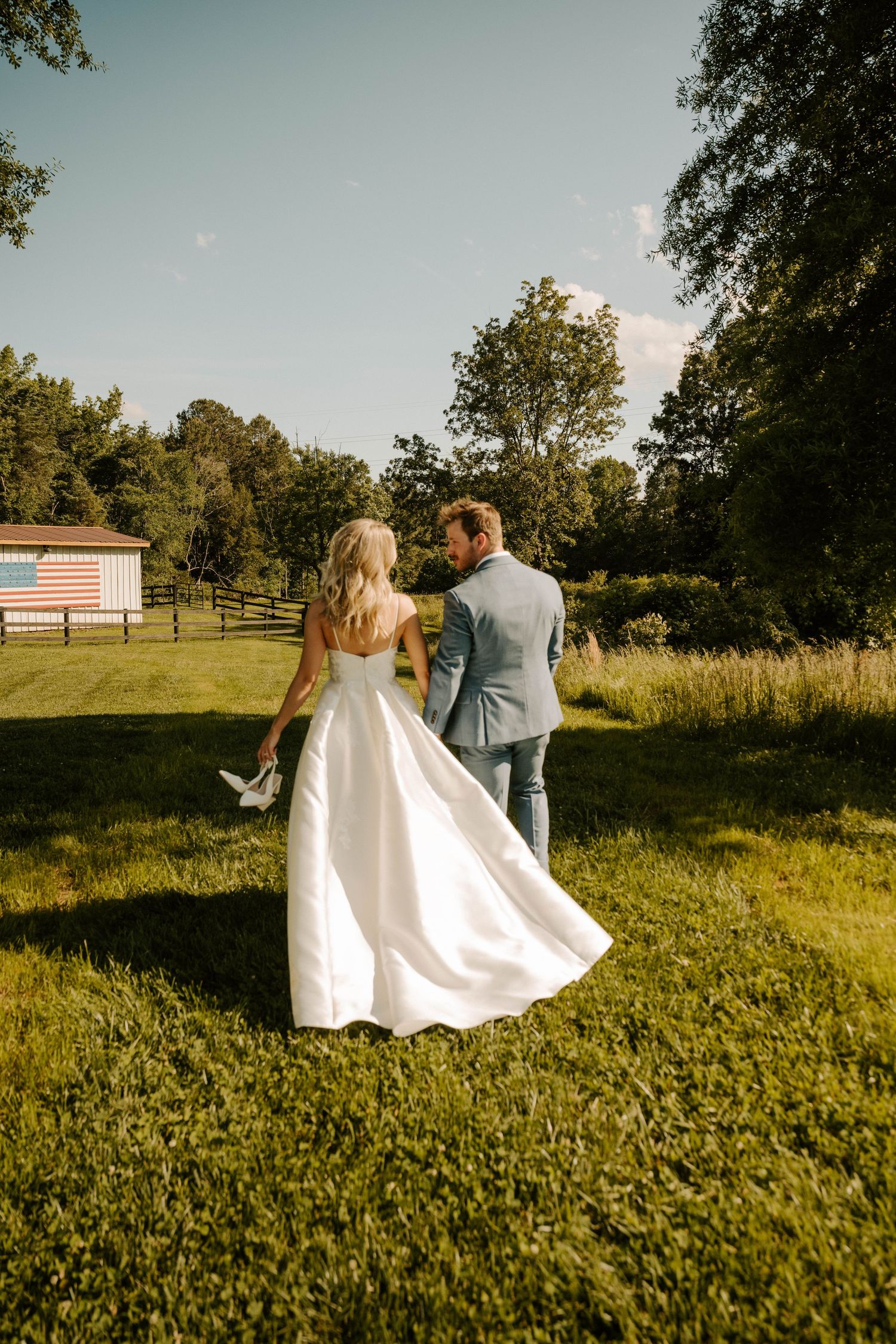 Newlyweds walking together on grass with a rustic barn in background during golden hour.