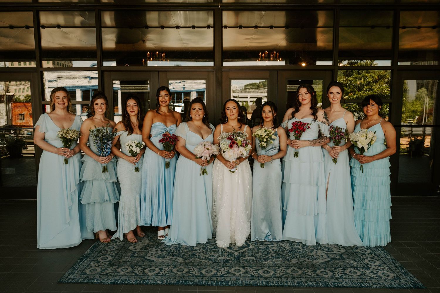 Wedding party wearing light blue bridesmaid dresses poses for group photos in formal outdoor setting.
