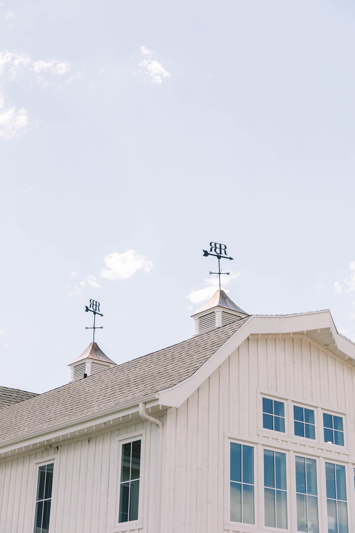 White barn-style building with twin weather vanes against light blue sky.