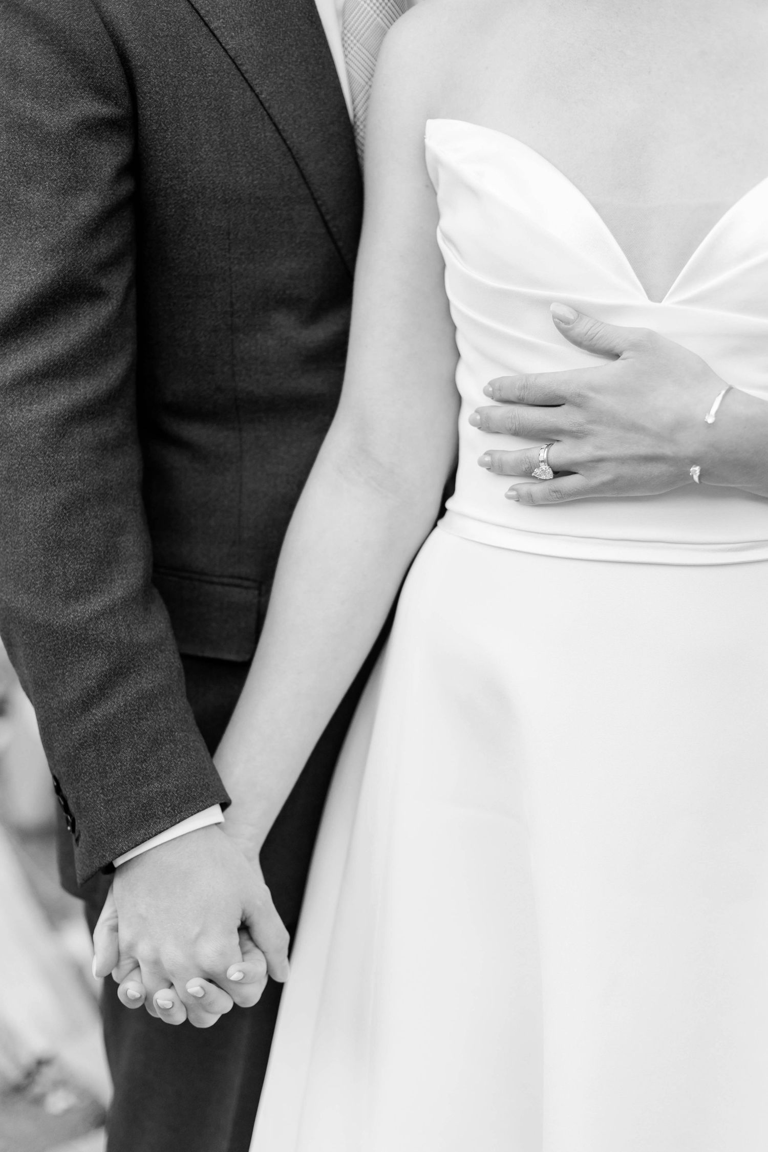 Black and white detail shot of couple holding hands, showing wedding dress and suit.