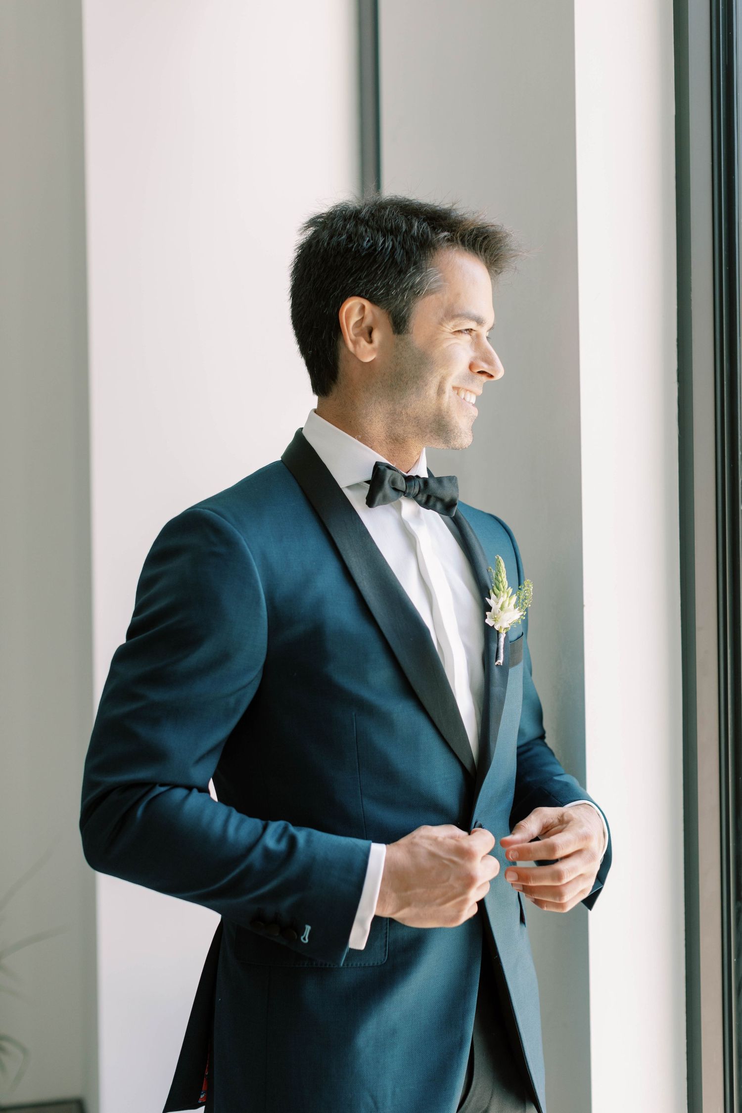 Formal attire featuring navy blue tuxedo jacket with boutonniere near window.