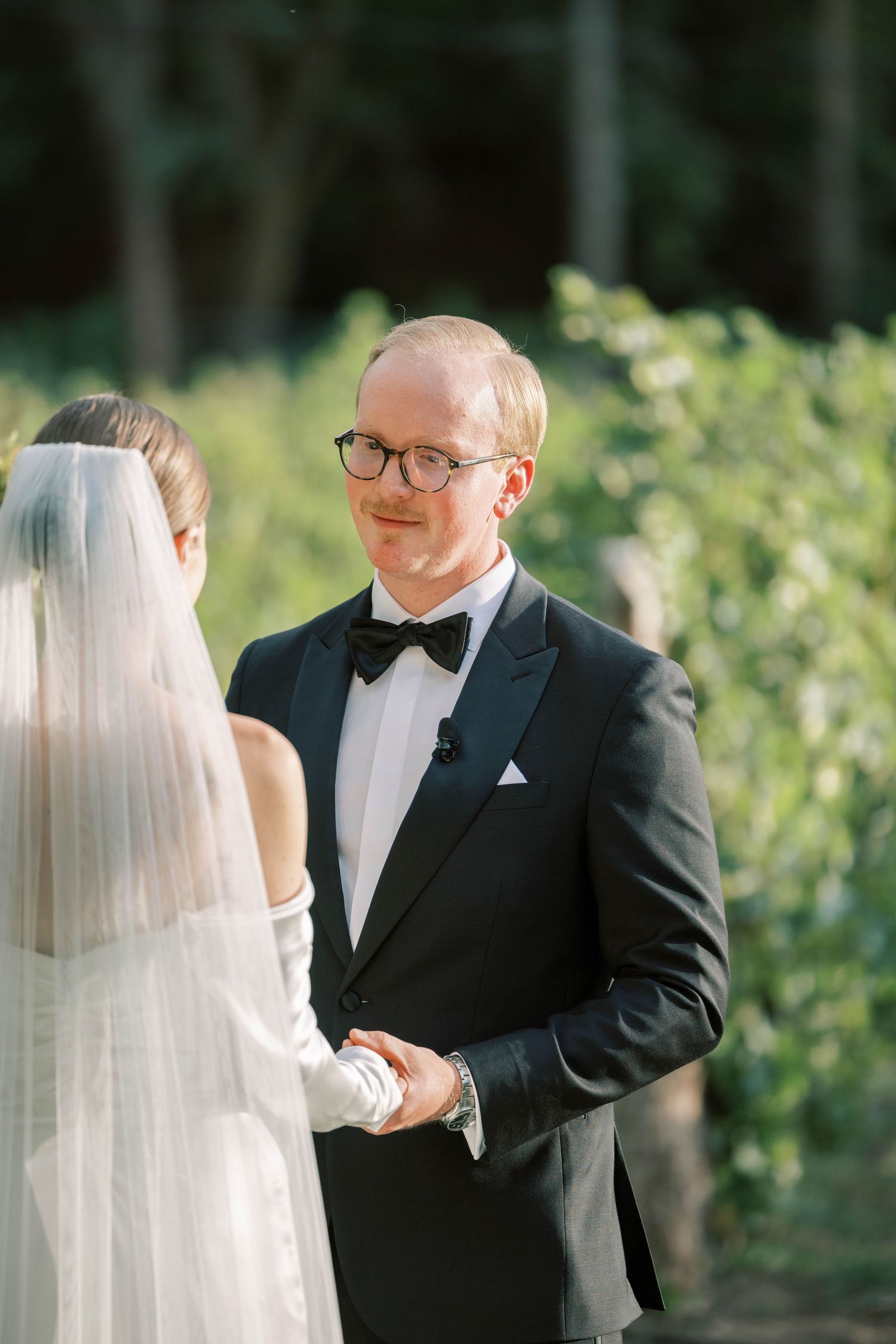 Intimate wedding ceremony moment captured during vow exchange with natural greenery in background.