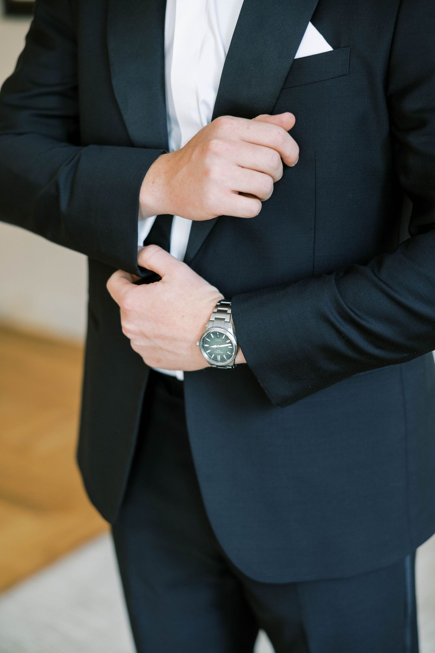 Close-up of hands adjusting black tuxedo jacket with visible luxury watch.