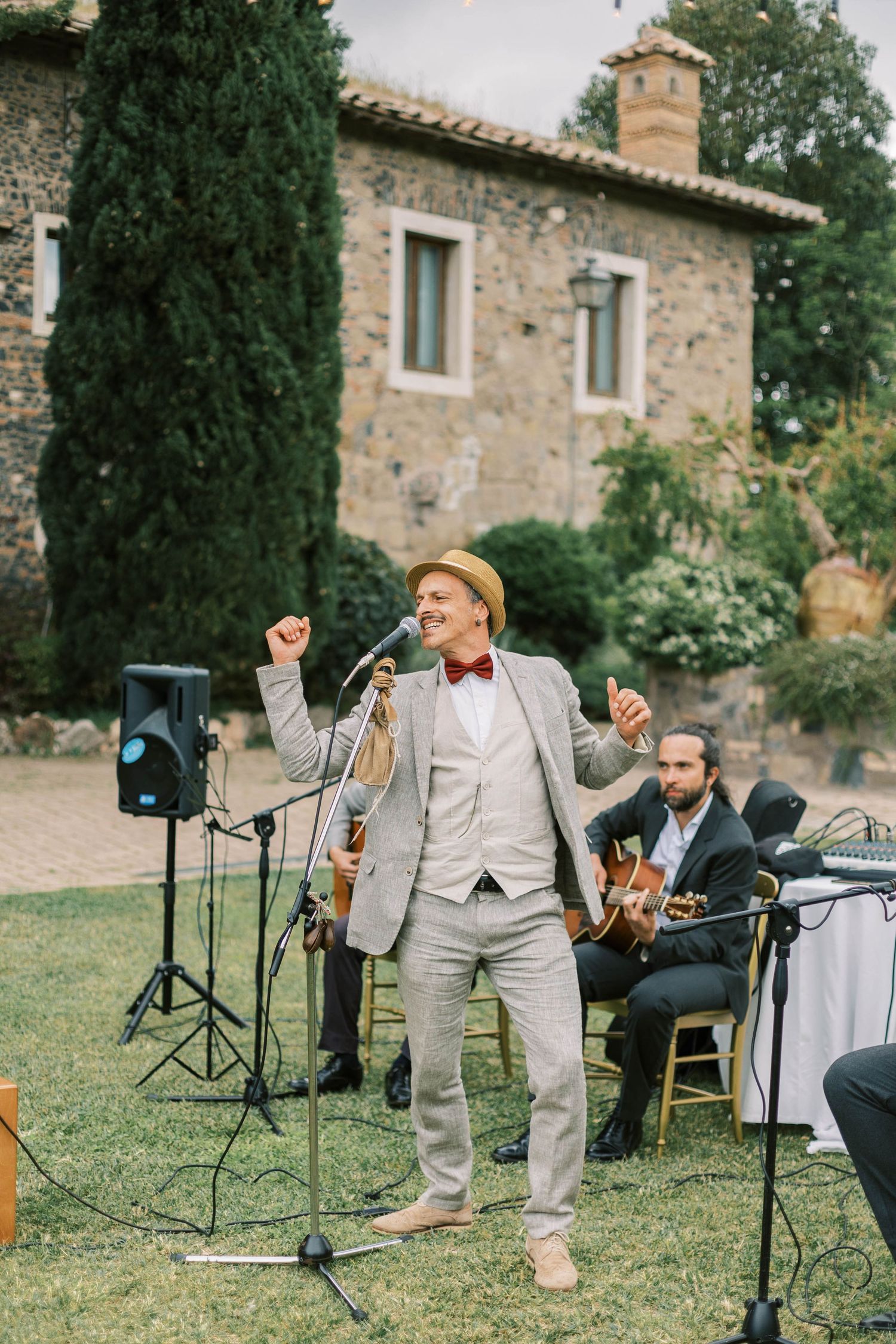 Wedding singer in light suit performs with band at outdoor Italian villa reception.