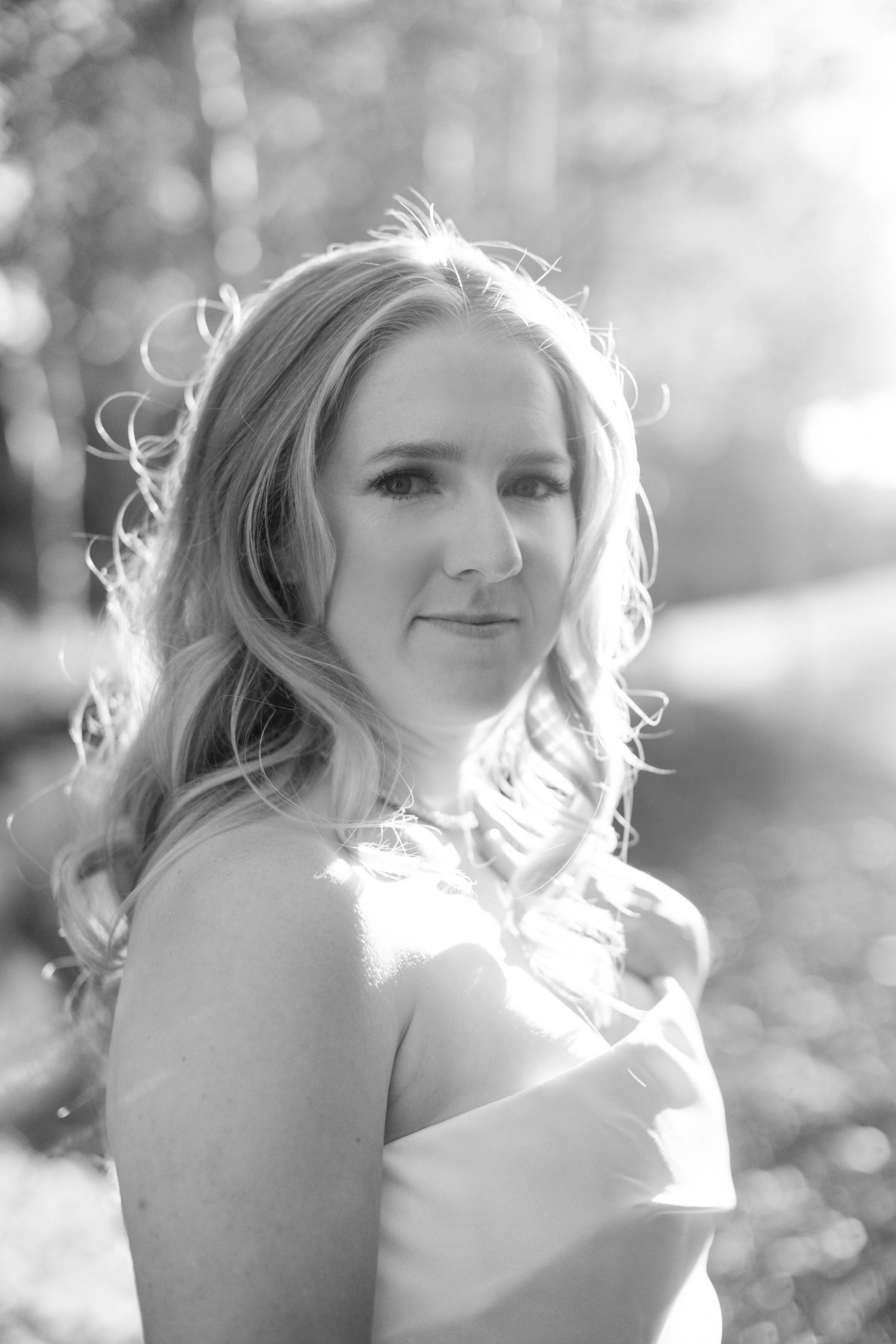 Backlit portrait of bride with flowing blonde hair in natural setting.