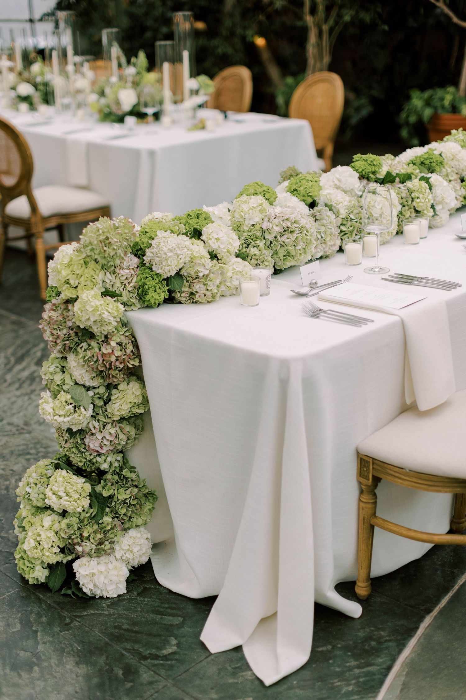 White hydrangea floral runner cascades off elegant wedding table with gold-backed chairs.