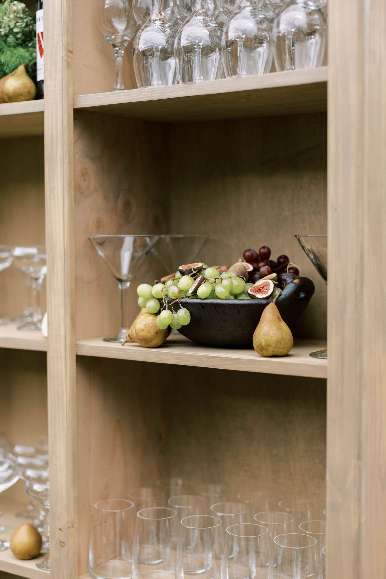 Wooden shelving displaying wine glasses and fresh fruit for elegant event setup.