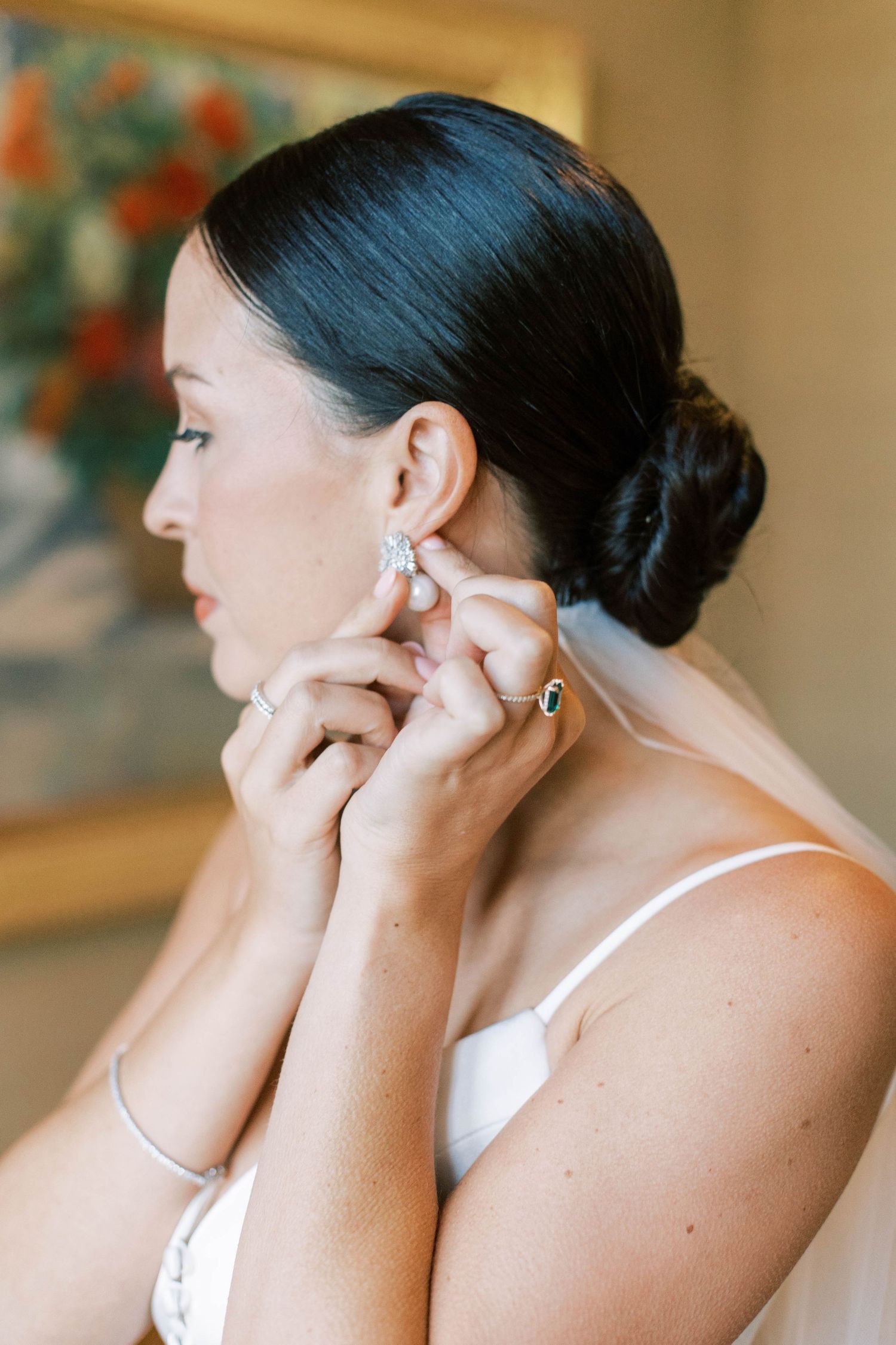 Side profile of bride putting on pearl earring while getting ready.