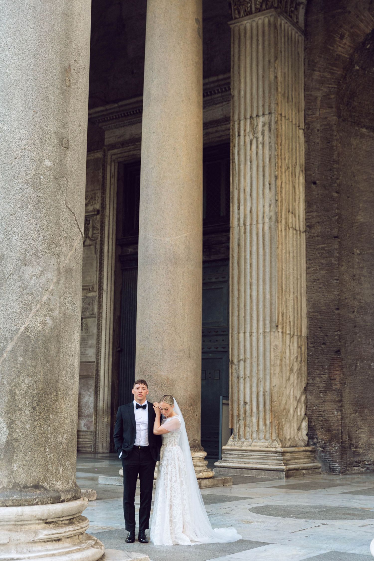 Wedding couple poses between towering classical columns at the historic Pantheon in Rome.