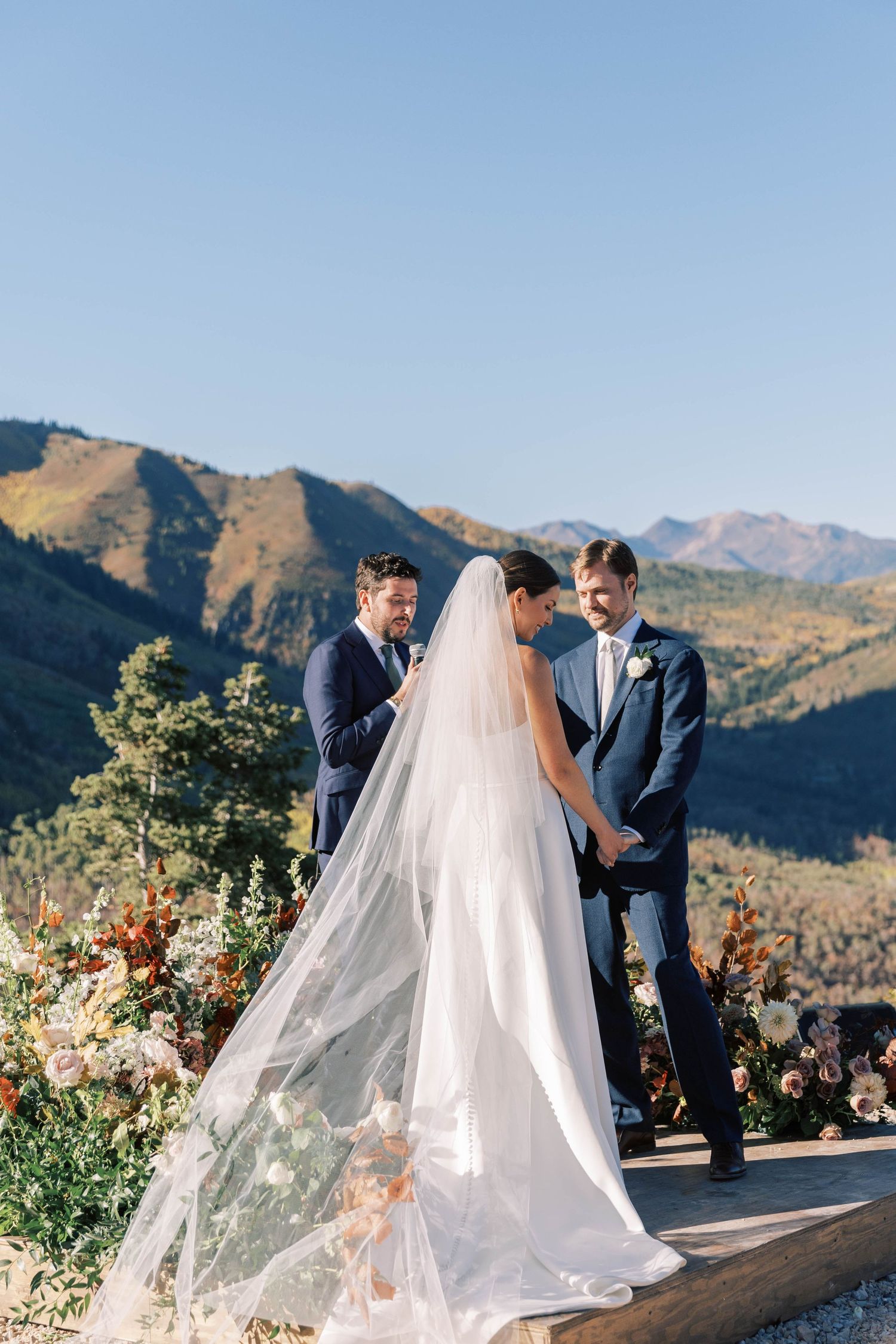 Wedding ceremony on mountain overlook with flowing veil and autumn floral arrangements.