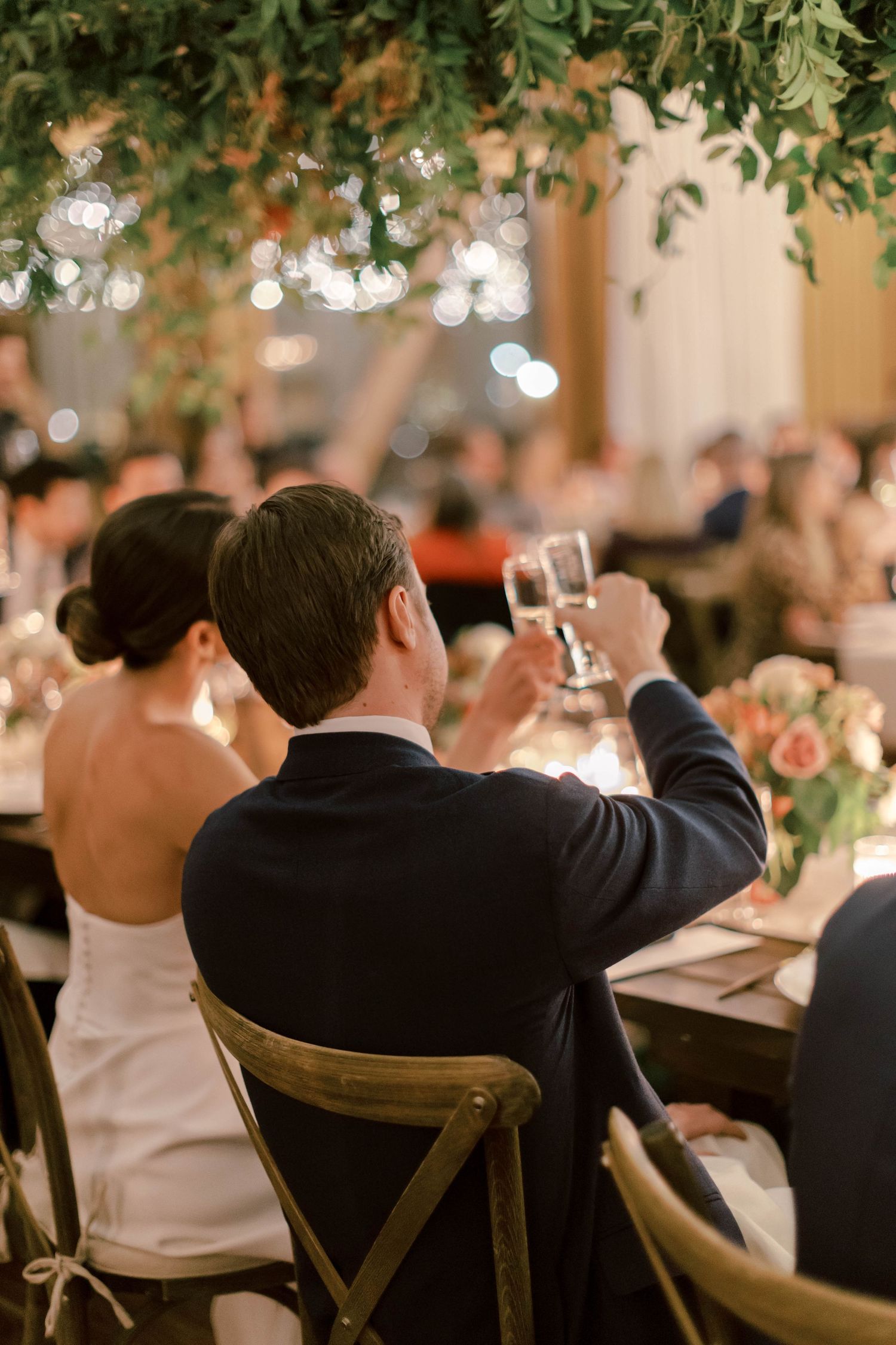 Wedding reception scene with toasting glasses and romantic bokeh lighting effects.