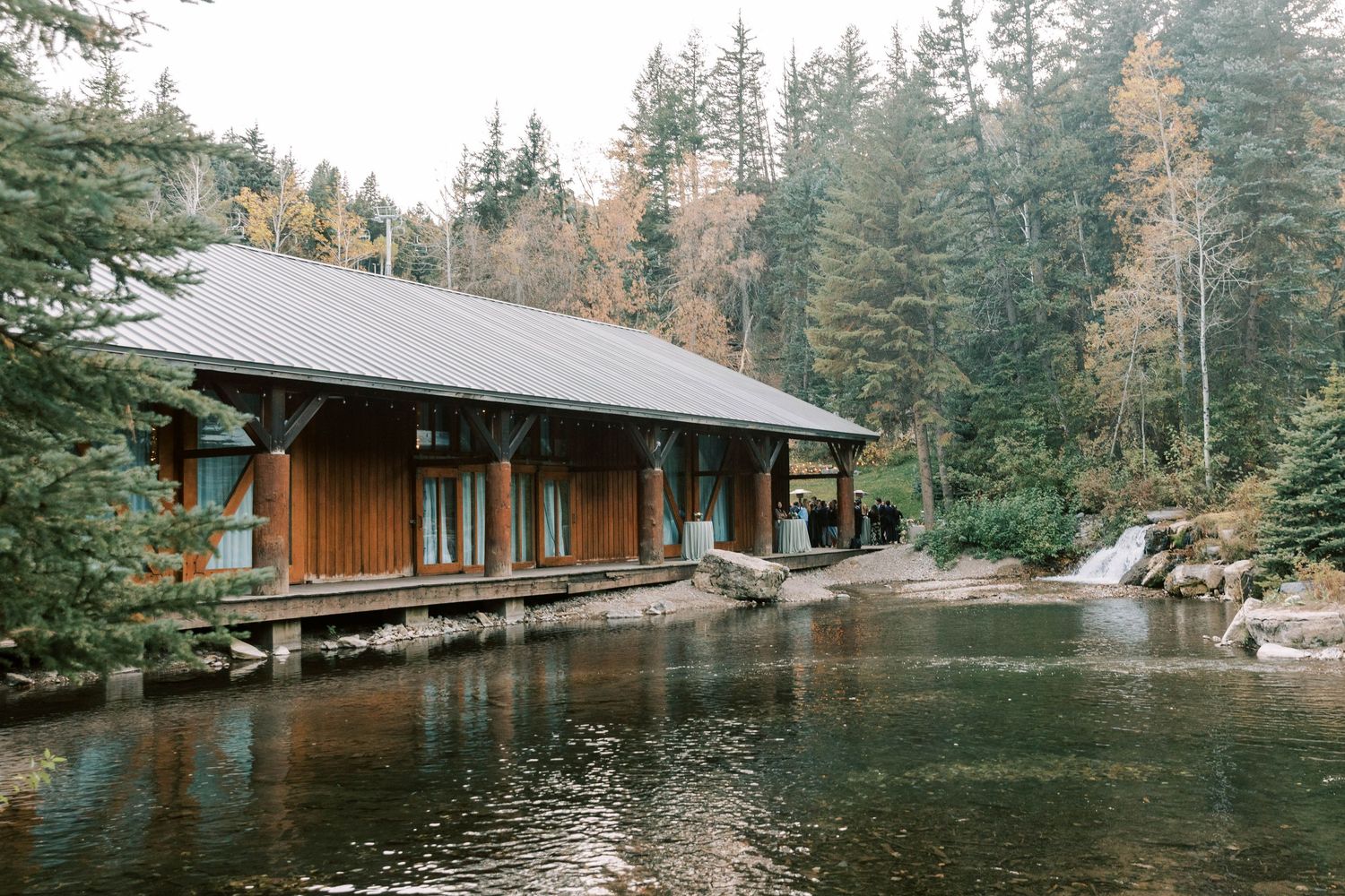 Rustic wooden lodge situated on the edge of a serene pond surrounded by evergreen forest.